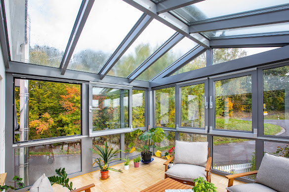 Verglaster Wintergarten mit Schiebefenstern und großen Schiebetüren in Aluminium, mit klarem Blick ins Grün und Licht durch die 3-fach Wärmeschutzverglasung.