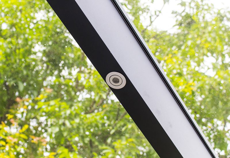 Integrierte LED-Spots mit schwarzem Rahmen in einem Wintergarten, dezente Punktlicht-Optik, Blick auf grüne Natur für stimmungsvolles Licht am Abend.
