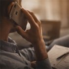 Hand mit Smartphone am Ohr, warmes Licht und unscharfe Unterlagen im Hintergrund bei Maul Wintergarten